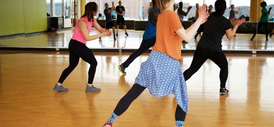 Voksne laver dansetrin med strakte ben i et spejlbeklædt træningslokale