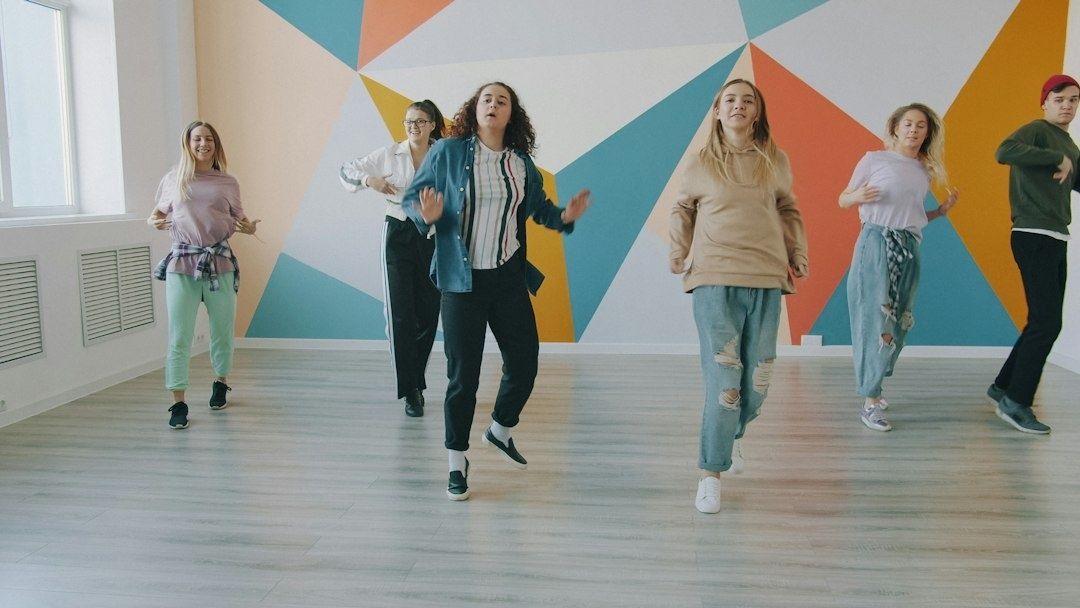 Seks personer øver dansetrin i et lyst lokale med farverig væg